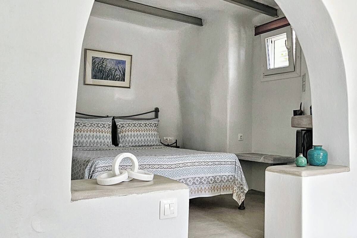 Een slaapkamer met een bed, een tafeltje, een raam en een deur.