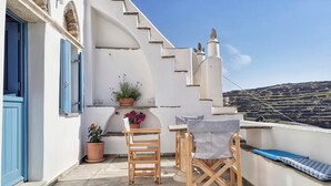 A balcony with a table and chairs, potted plants, and a view of a hilly landscape. - Tinoshomelidays Residences (Tinos)
