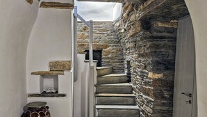 A narrow staircase with stone steps leading to a door, a white wall, and a rustic wooden pot on the floor. - Tinoshomelidays Residences (Tinos)