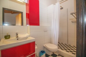 A bathroom with a red sink, white toilet, and a shower with a checkered floor.