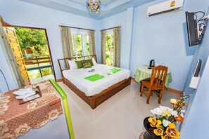 A bedroom with a bed, a desk, and a chair. There is a window with curtains, a table with a chair, and a vase with flowers. - Rat Villa (Pa Klok)
