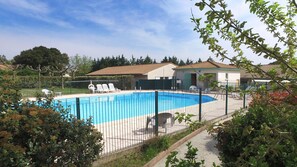 Una piscina con área vallada, rodeada de vegetación y un edificio con tejado de baldosas.