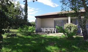 Une maison dotée d’un patio comprenant une table et des chaises, le tout entouré de verdure et d’arbres.
