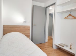 A bedroom with a bed, a door, a hallway, and a shelf with a book and reed diffuser.