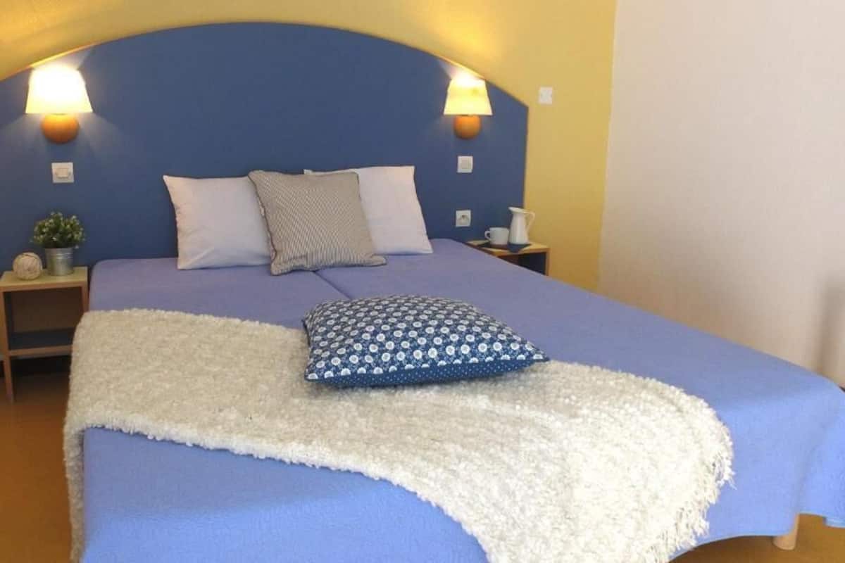 A bed with a blue headboard, two bedside lamps, a white throw blanket, and a patterned pillow.