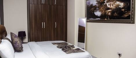 A bedroom with a bed, a wardrobe, a painting, and a bedside table with a lamp.