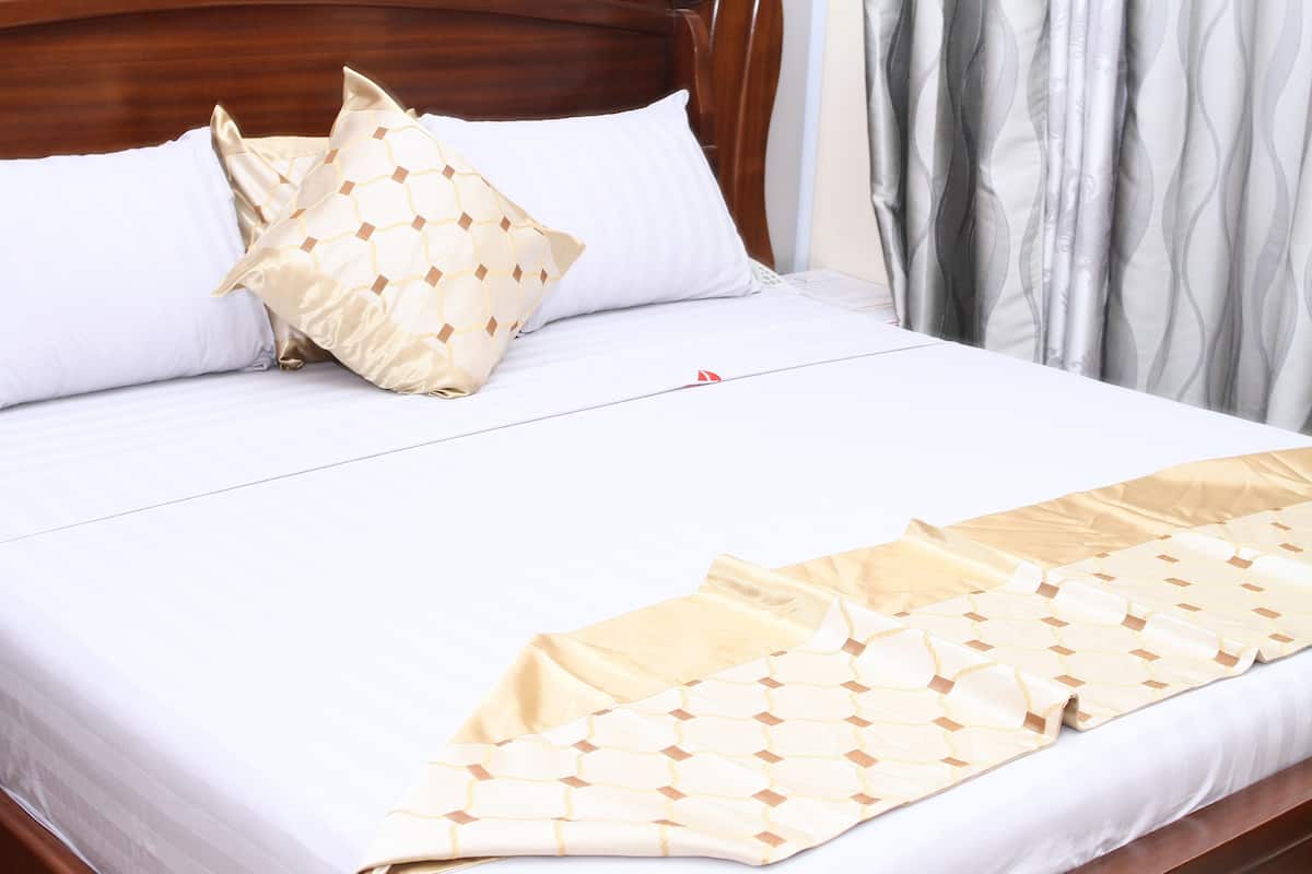 Una cama bien tendida con ropa de cama blanca y un edredón con motivos dorados.