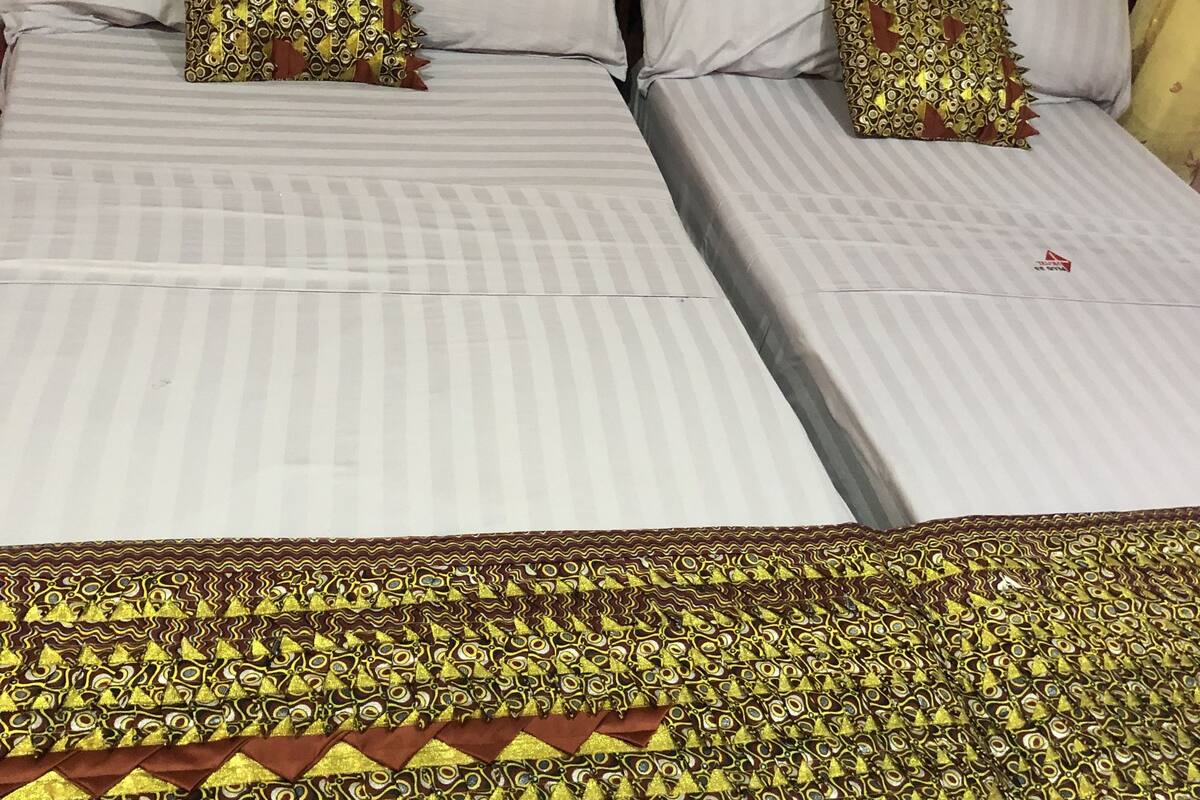 Dos camas individuales con sábanas blancas y almohadas estampadas, un cabecero de madera y una pared roja con un interruptor de luz.