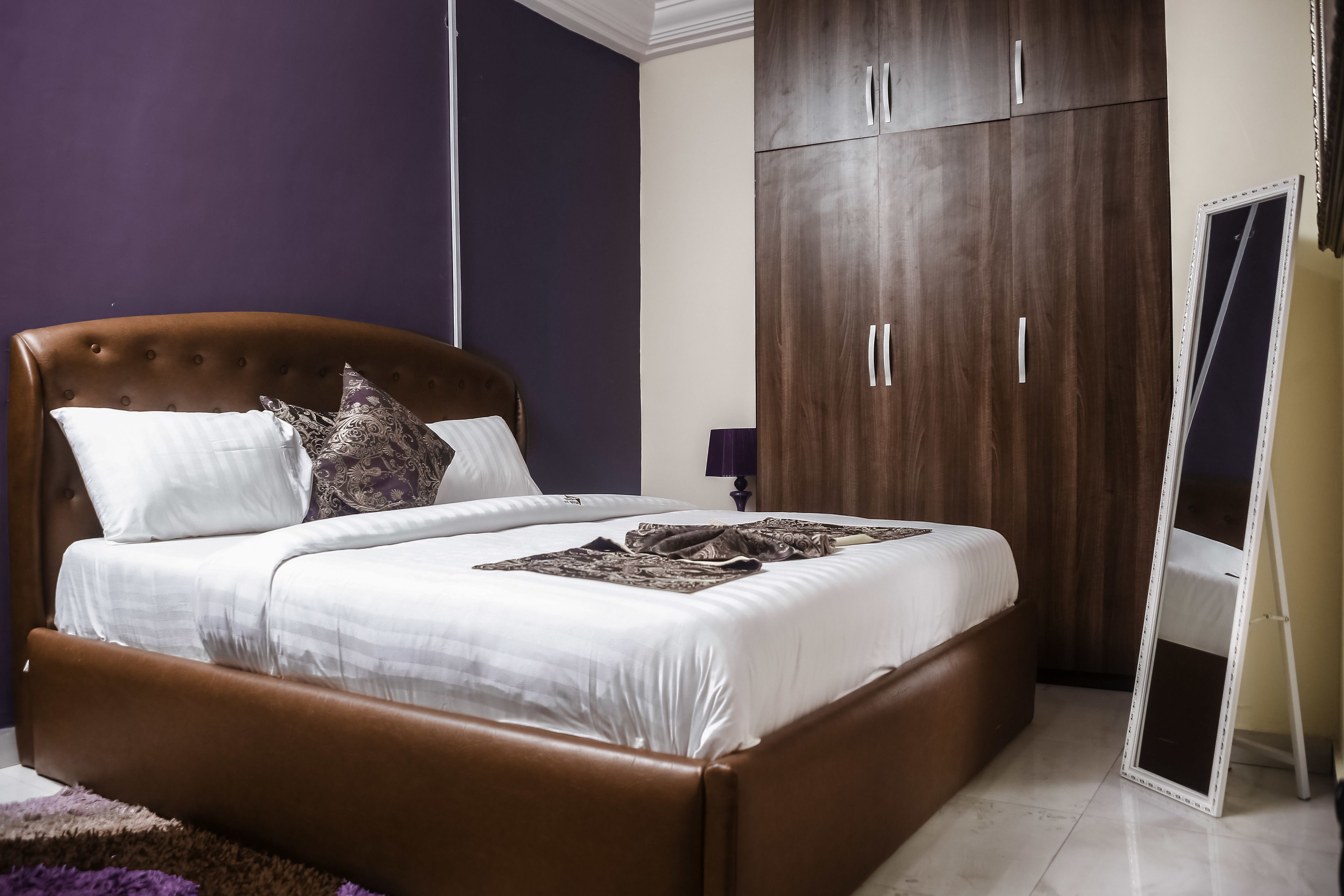 A bedroom with a brown upholstered bed, white bedding, and a large wardrobe.
