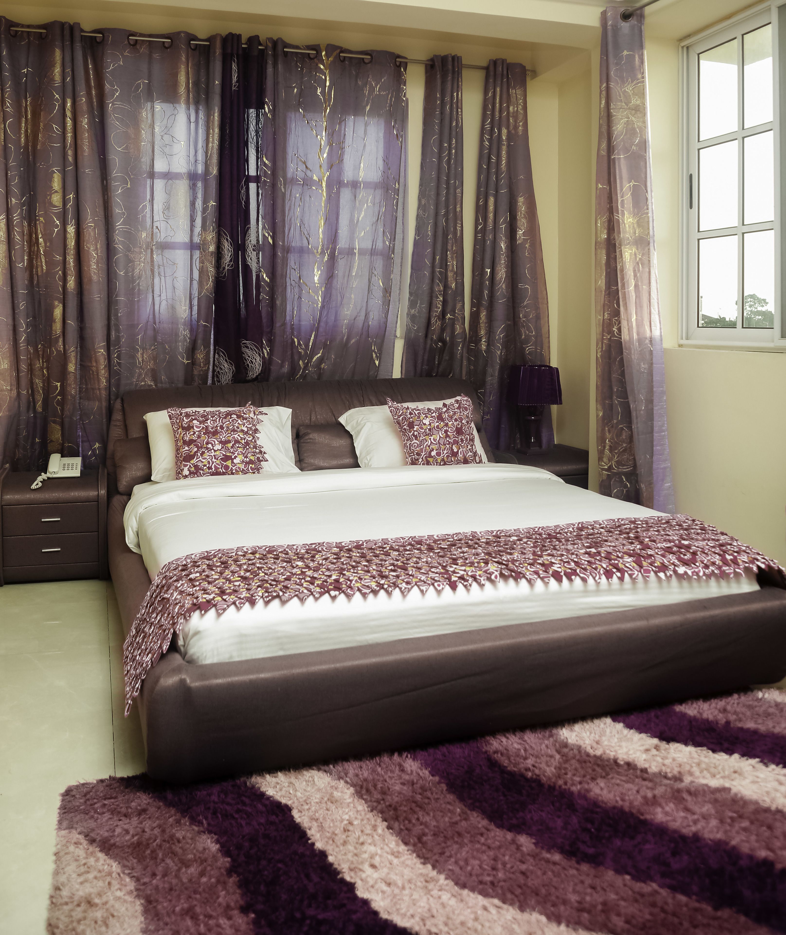 A bedroom with a large bed, a bedside table with a lamp, and curtains.