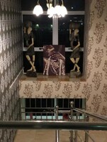 Uma escadaria com corrimão, papel de parede estampado e uma janela com duas estátuas e um quadro emoldurado.