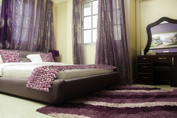A bedroom with a large bed, purple curtains, a dresser, and a painting on the wall.
