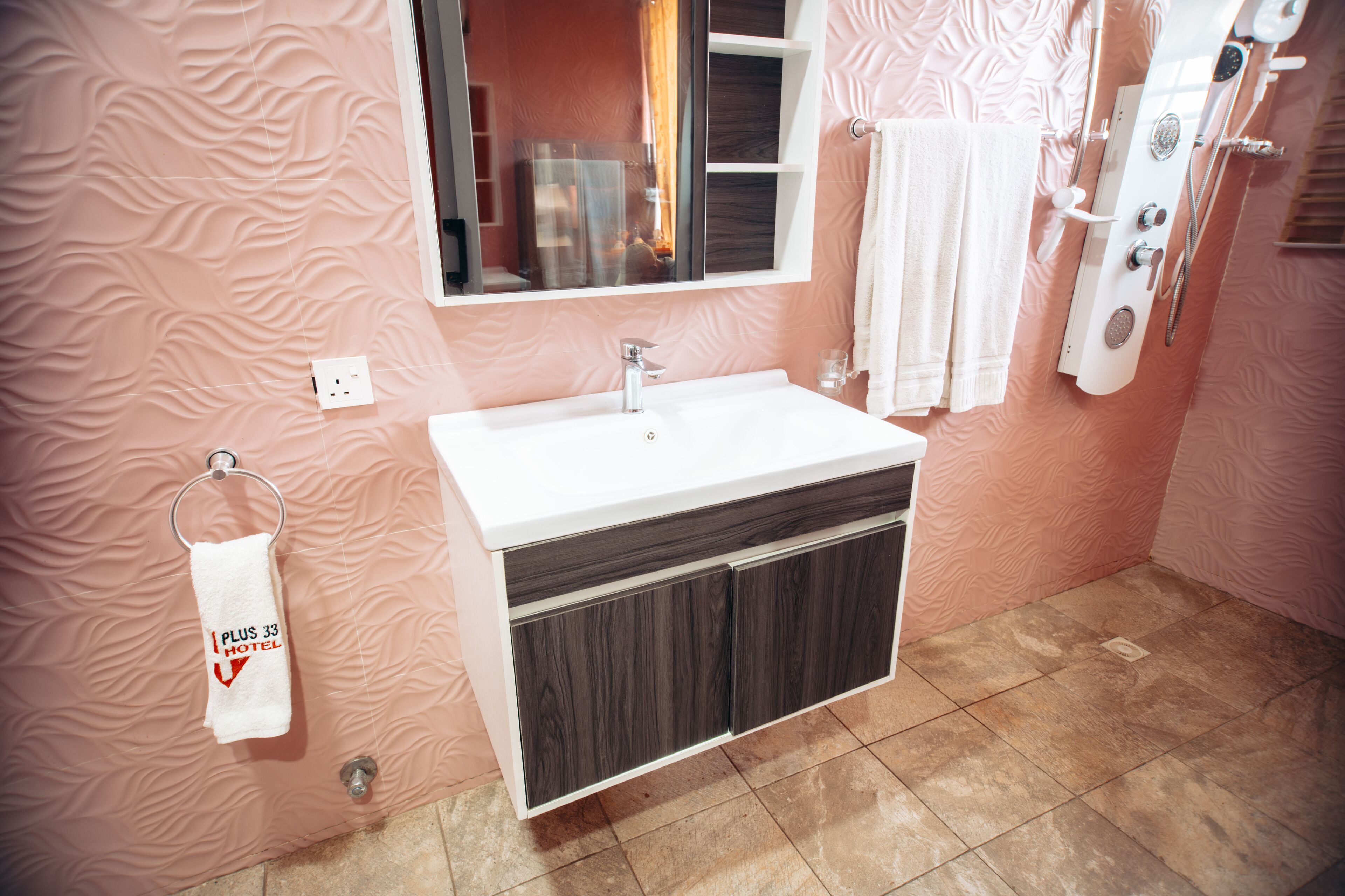 Un baño con lavamanos blanco, armarios de madera oscura, un perchero y una zona de ducha.