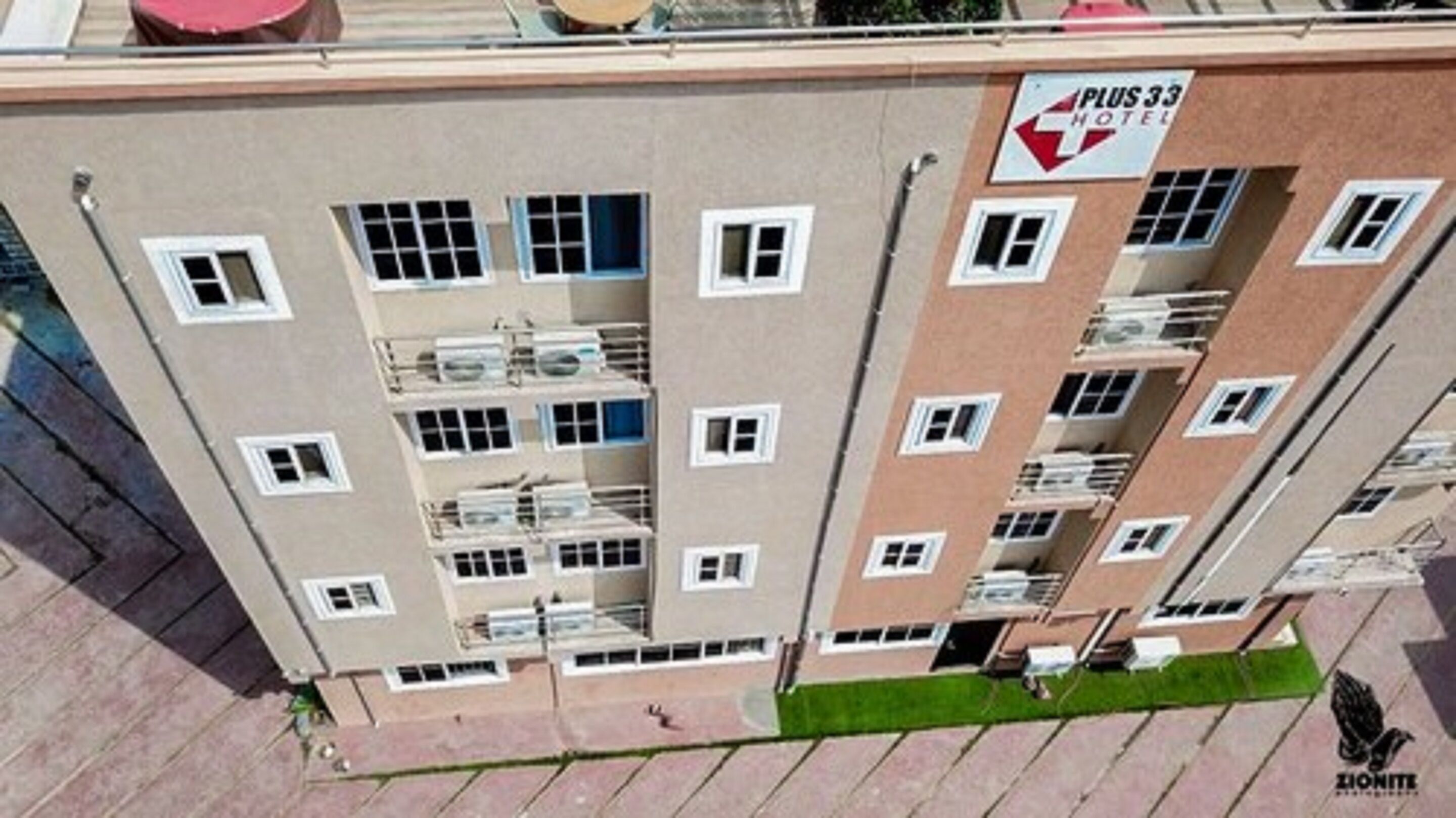 A multi-story hotel building with balconies, a sign indicating it is a Plus 33 Hotel, and a logo for Zionite.