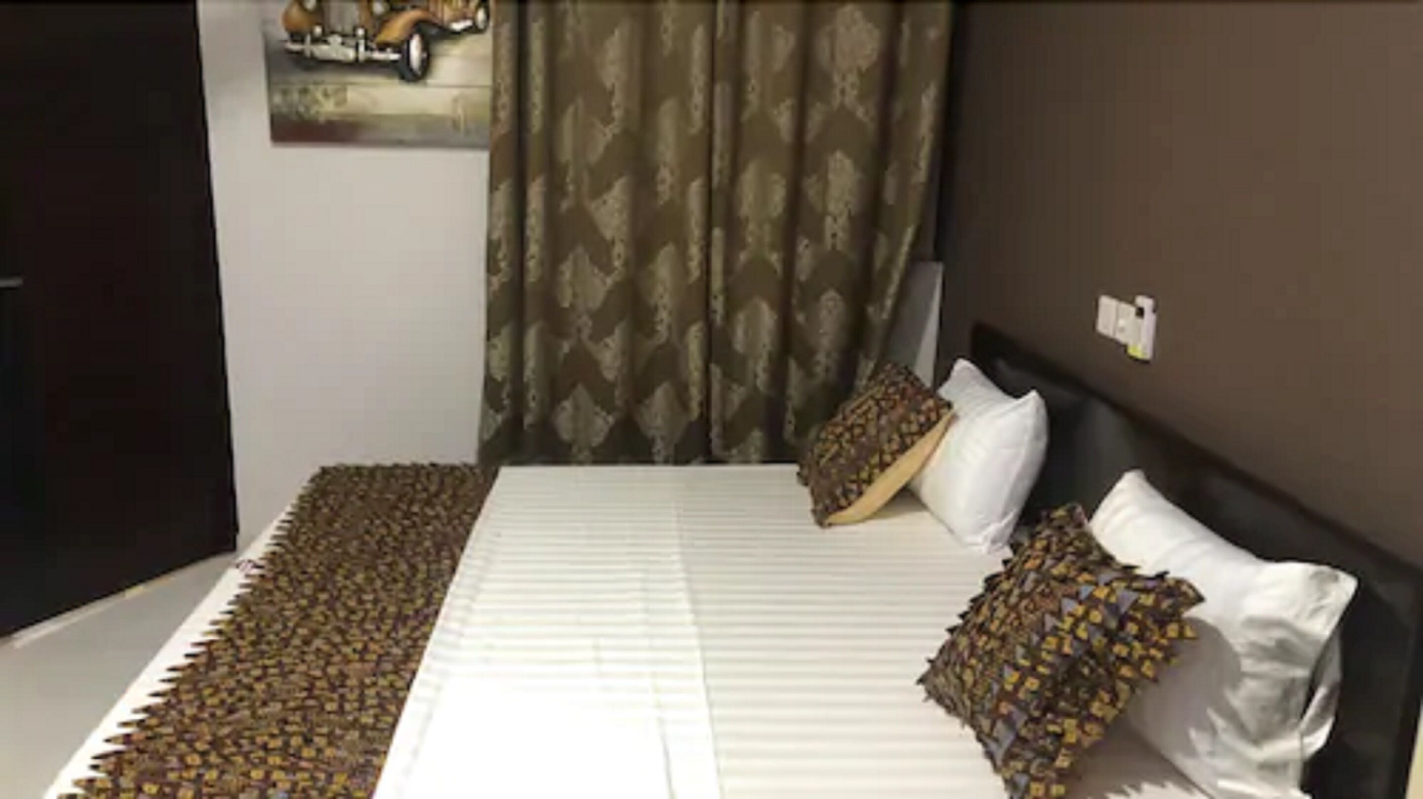 Un dormitorio con cama, almohadas, una colcha, un cuadro en la pared y cortinas.