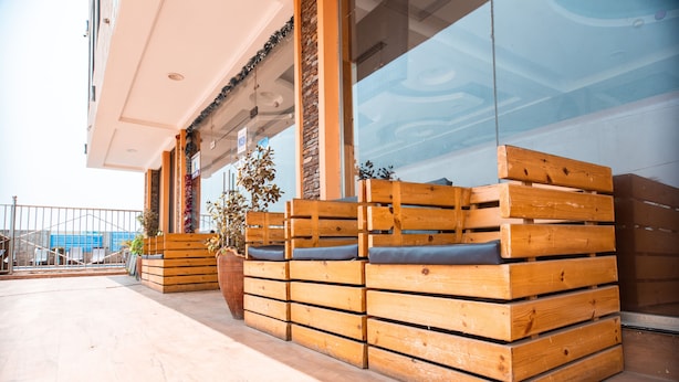 Un banc en bois avec des coussins, placé à l’extérieur d’un bâtiment doté de grandes fenêtres.