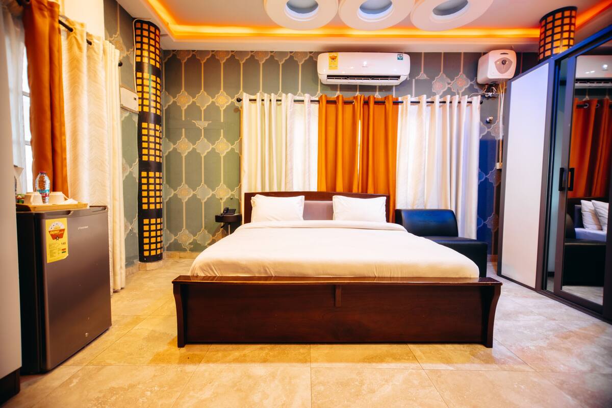 Habitación de hotel con una cama grande, un escritorio con refrigerador, una silla y un armario con puerta corredera.