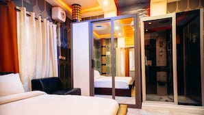 Une chambre d’hôtel comprenant un lit, un banc, un espace douche et une porte en verre donnant sur une salle de bain.