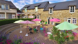 Une cour bordée de bâtiments en pierre, avec des espaces de repos en plein air et des parasols.