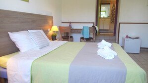 Un lit bien fait, avec des oreillers et une couverture, une lampe de chevet, une chaise, une petite table avec une serviette et un réfrigérateur.