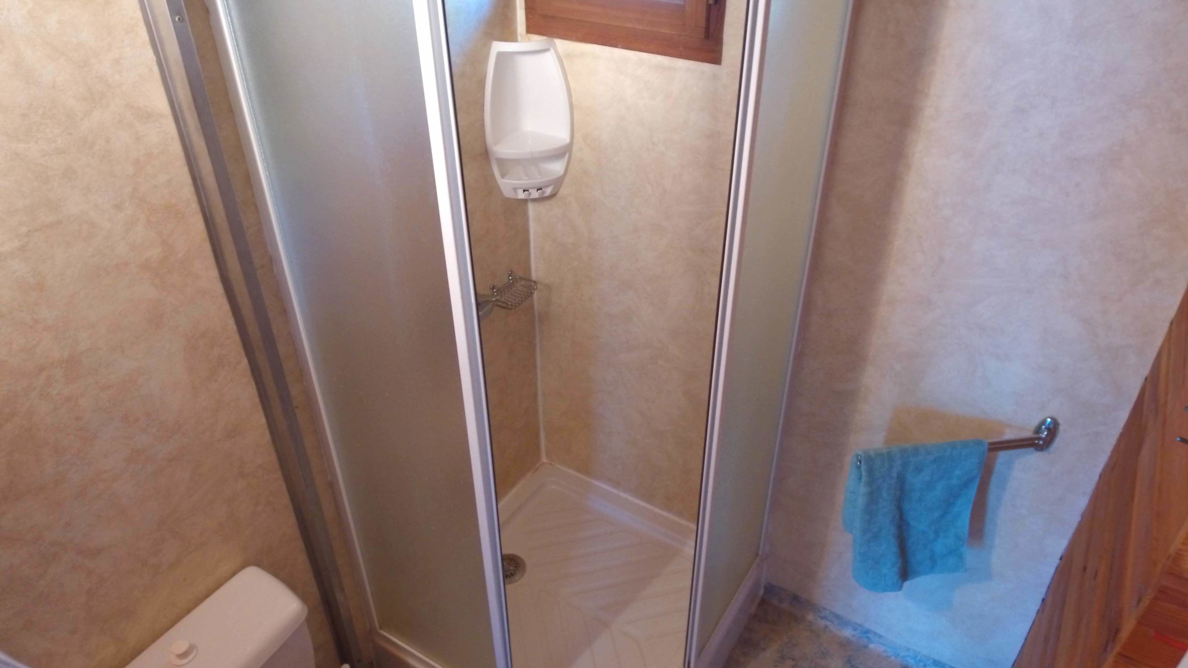A small, enclosed shower area with a glass door, a white toilet, and a towel hanging on a hook.