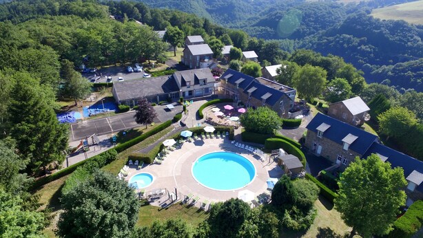 Vue aérienne d’un complexe hôtelier comprenant plusieurs bâtiments, une piscine centrale et une végétation luxuriante.