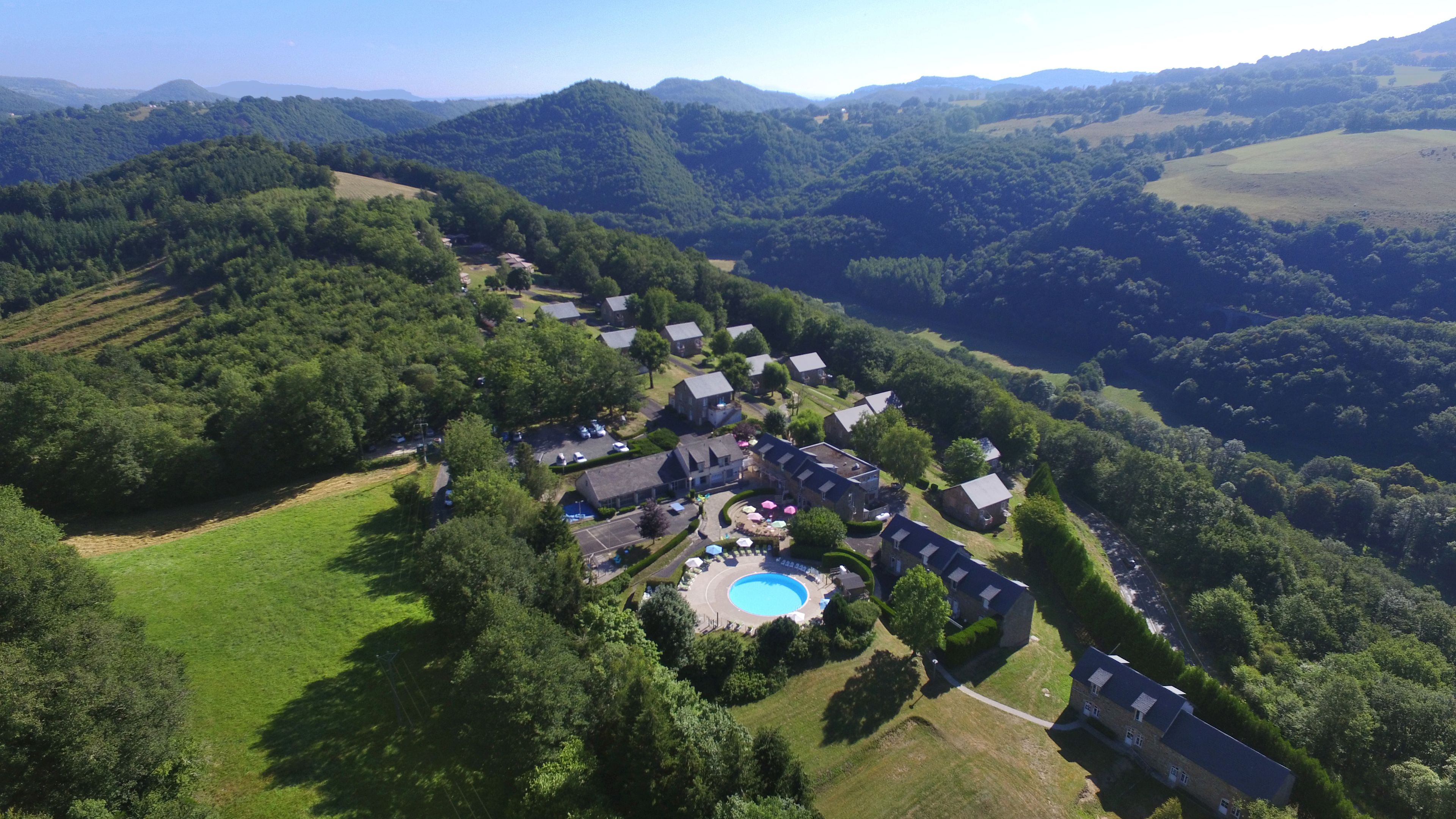 Vue aérienne d’un quartier résidentiel avec des maisons, une piscine et de la végétation environnante.