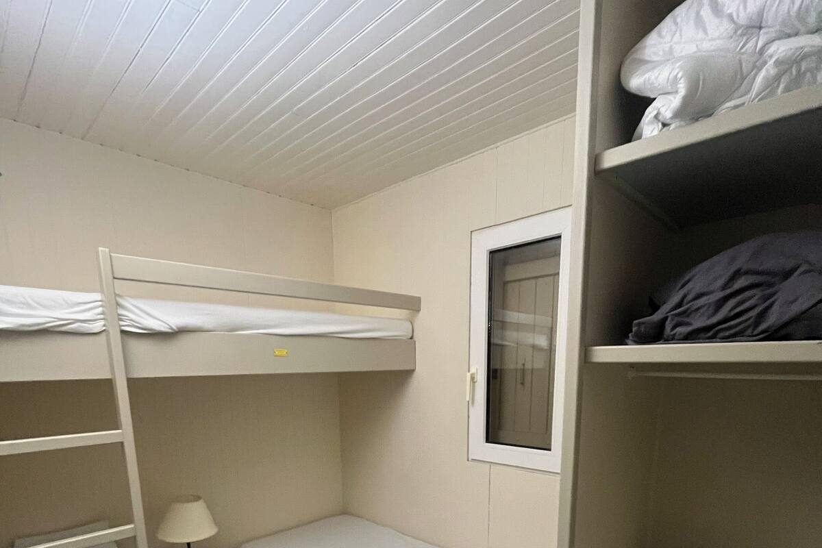 Une chambre avec un lit superposé, une fenêtre, une table de chevet avec une lampe et une chaise.