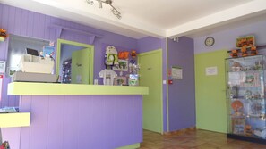Zona de recepción con mostrador, espejo, reloj de pared y vitrina de vidrio con juguetes.