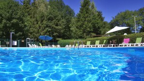 Une piscine à l’eau d’un bleu cristallin, entourée de chaises longues et de parasols, avec des arbres en arrière-plan.