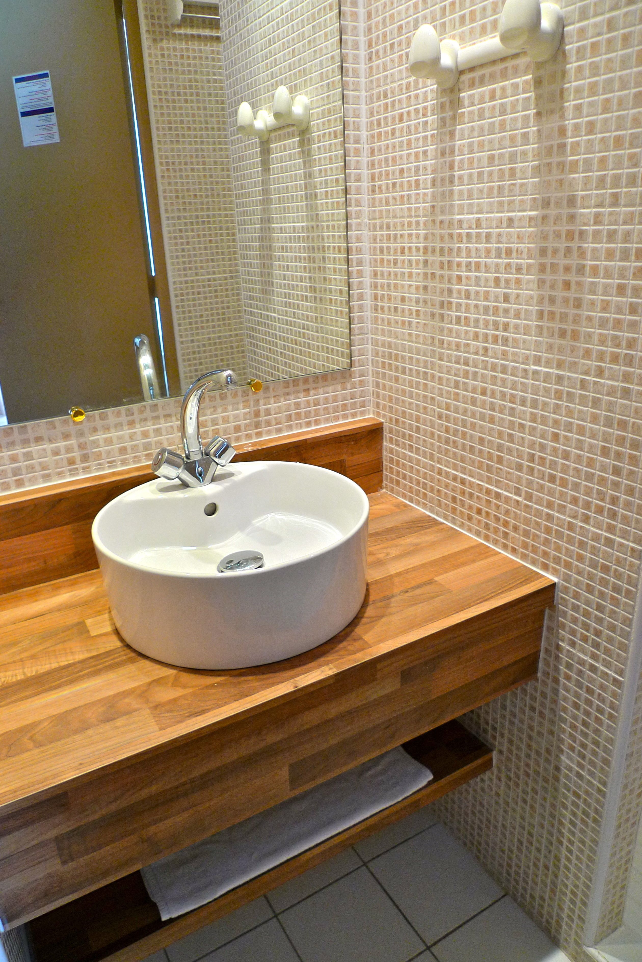 Ein Badezimmer mit einem weißen Waschbecken, einem Holz-Waschtisch, gefliesten Wänden und einem Spiegel.