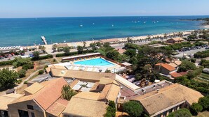 An aerial view of a coastal resort with a swimming pool, beach, and clear blue sea.
