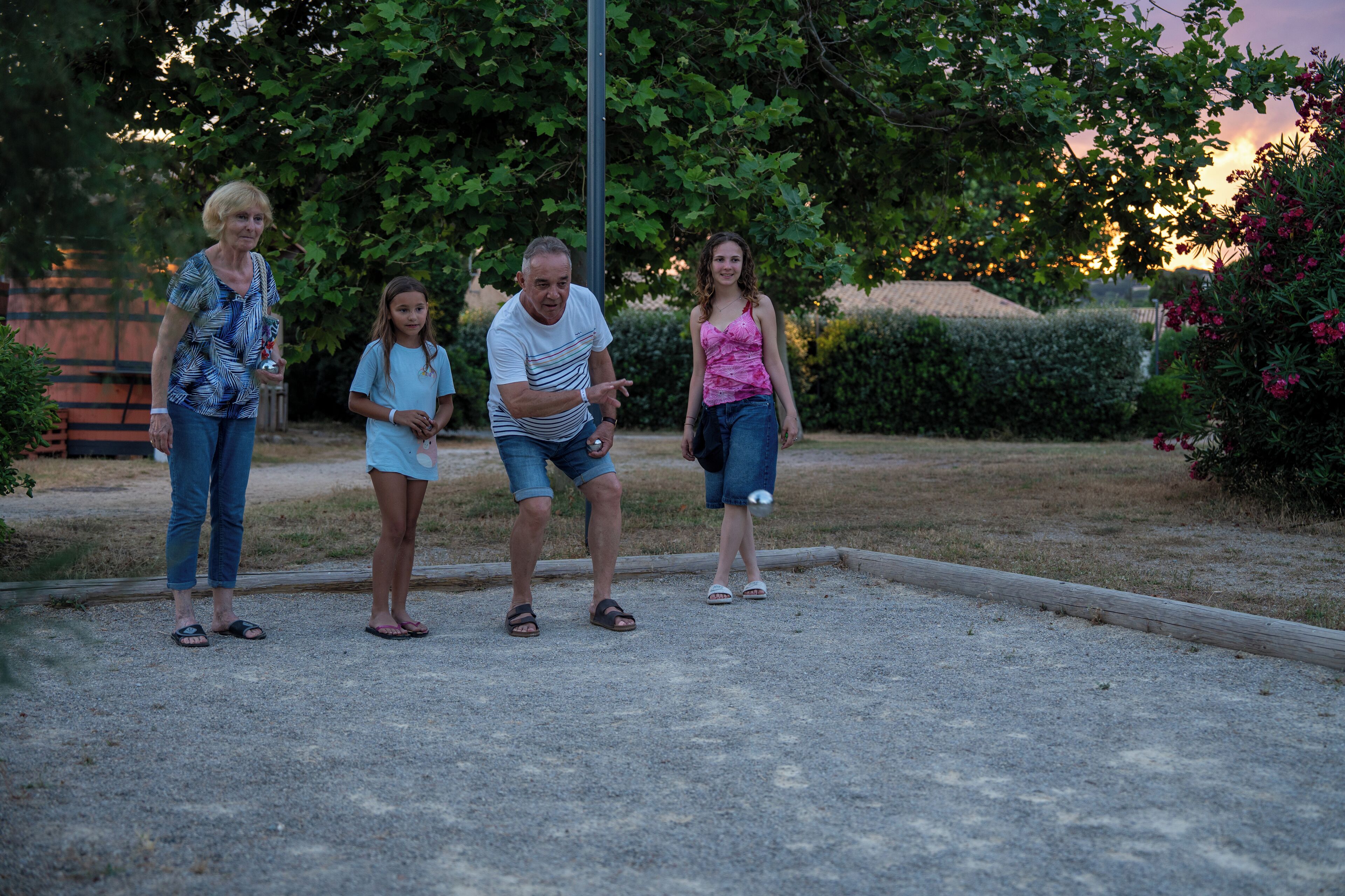 A family of four standing in a courtyard with a gravel ground, surrounded by greenery and a wooden fence.