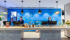 A reception desk with two staff members, a digital display, and a blue wall with travel-themed graphics. - Ibis Chongqing Jiefangbei Pedestrian Street Hotel (Chongqing)