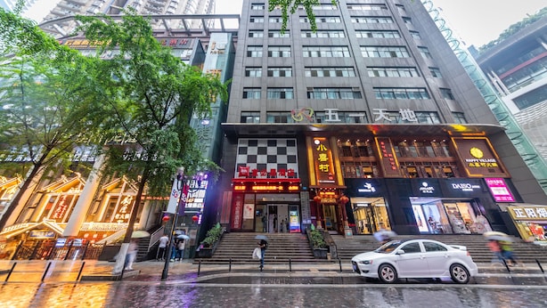 A multi-story hotel with a prominent entrance, multiple shops on the ground floor, and a white car parked in front. - Ibis Chongqing Jiefangbei Pedestrian Street Hotel (Chongqing)