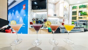 Three martini glasses with different colored drinks on a table in a modern bar area with a blue wall and a TV in the background. - Ibis Chongqing Jiefangbei Pedestrian Street Hotel (Chongqing)