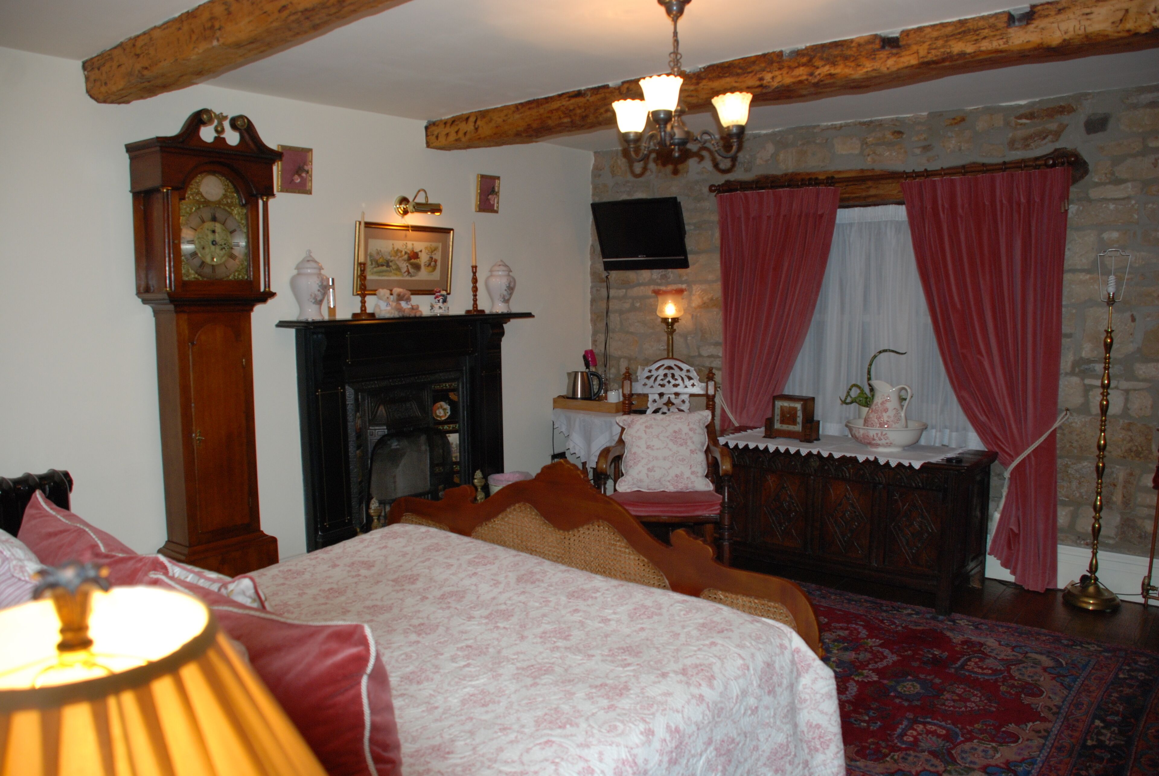 A traditional room with a fireplace, a large bed, a wooden ceiling, and a chandelier.