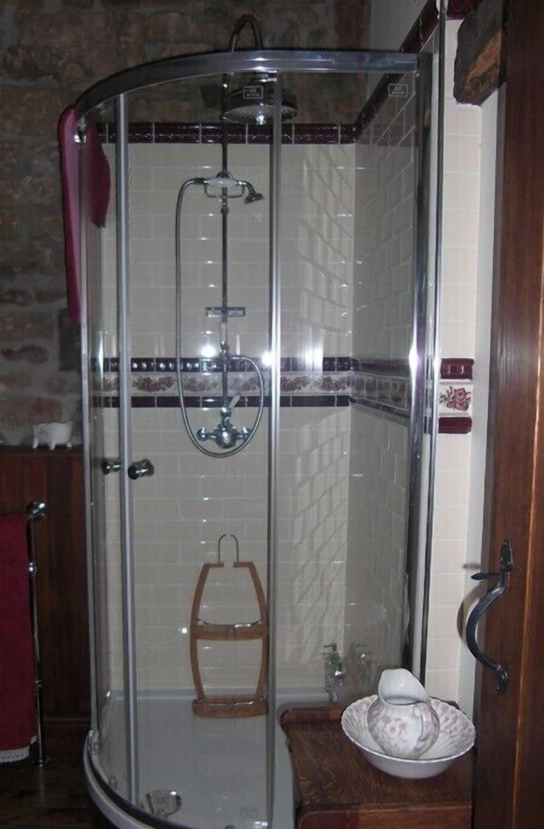 A glass-enclosed shower with a handheld showerhead, a towel rack, and a small wooden stool.
