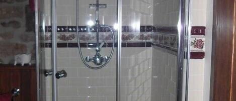 A glass-enclosed shower with a handheld showerhead, a towel rack, and a small wooden stool.