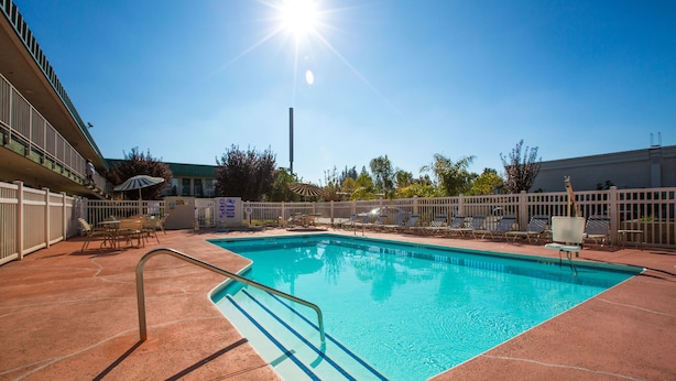 A rectangular swimming pool with a metal ladder, surrounded by a white fence, and a clear blue sky above.