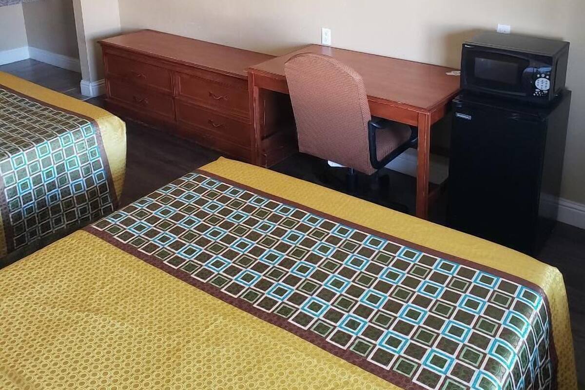 Habitación de hotel con dos camas, un escritorio, una silla, un televisor y un microondas.