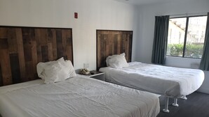 A hotel room with two beds, wooden headboards, white bedding, a bedside telephone, and a window with curtains.