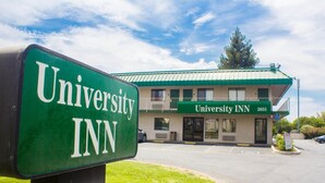 A University Inn sign and building with a green and white color scheme, a parking lot, and a clear sky.