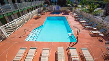 Una piscina con tumbonas y un área cercada, rodeada por un edificio con varios balcones.