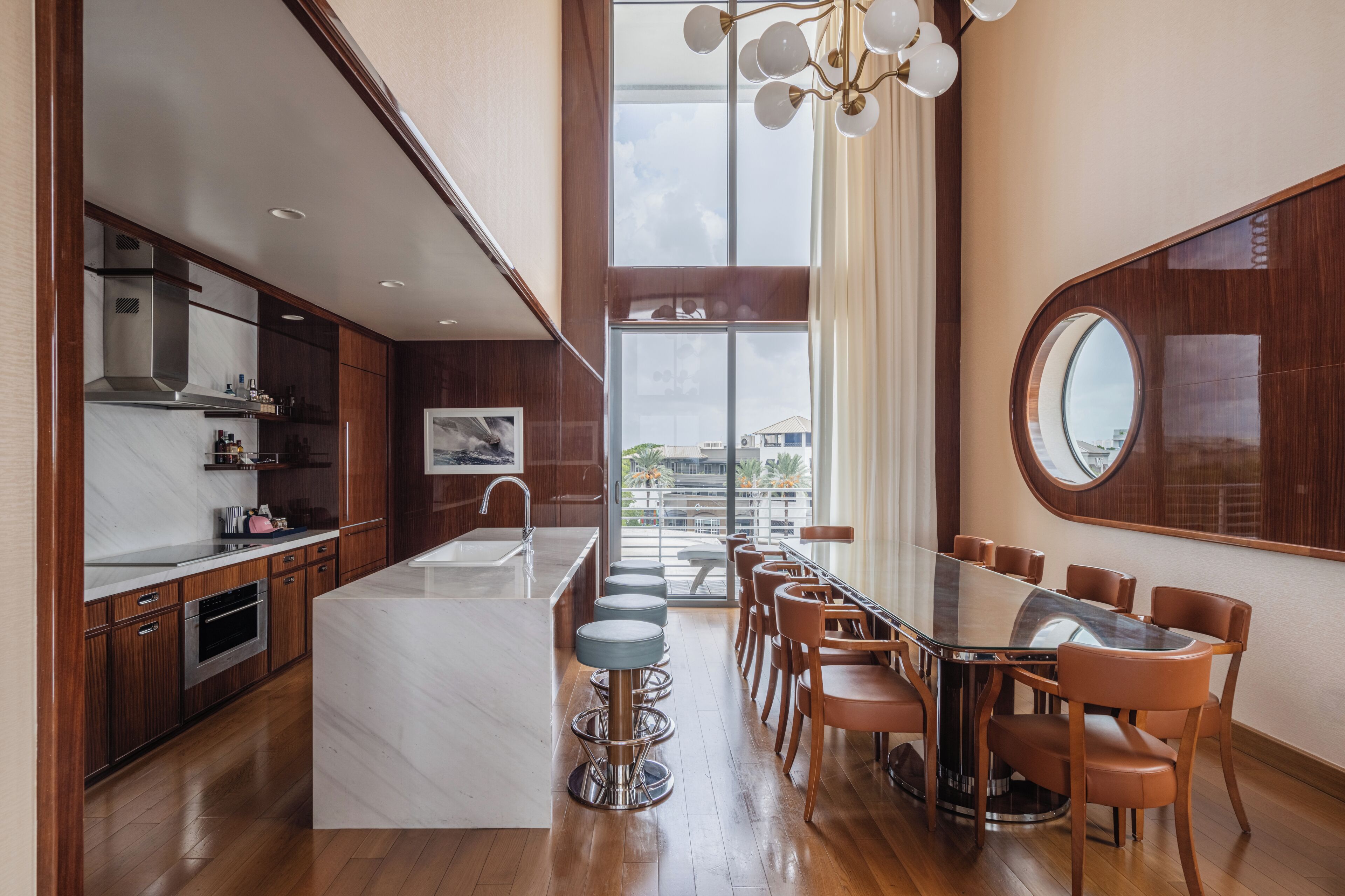 A modern kitchen with a central island, bar stools, and a dining area with a glass table and chairs.