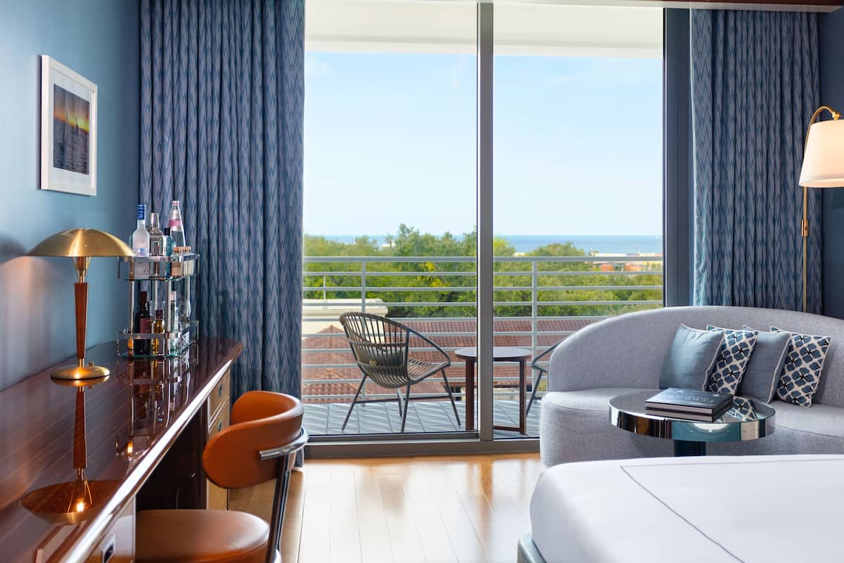 A hotel room with a balcony, a sofa, a coffee table, a bar area, and a view of the ocean.