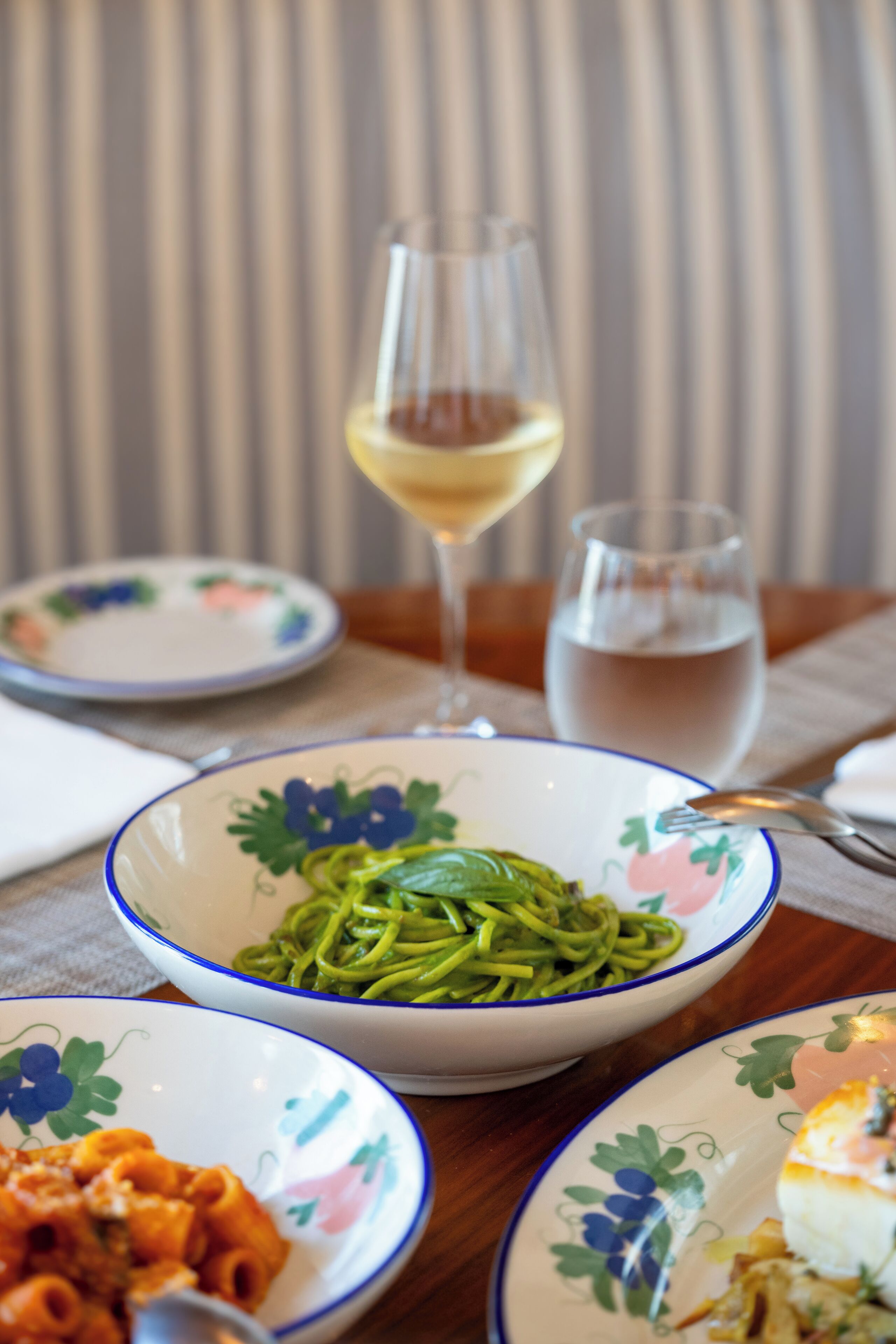 A dining table with various dishes, including pasta and a glass of white wine.