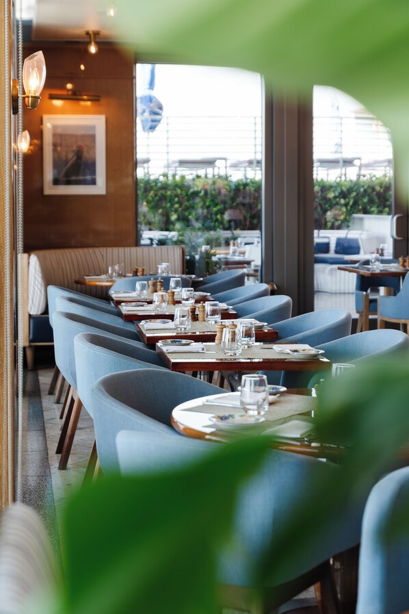 A restaurant with blue upholstered booths, wooden tables, and a view of greenery outside.