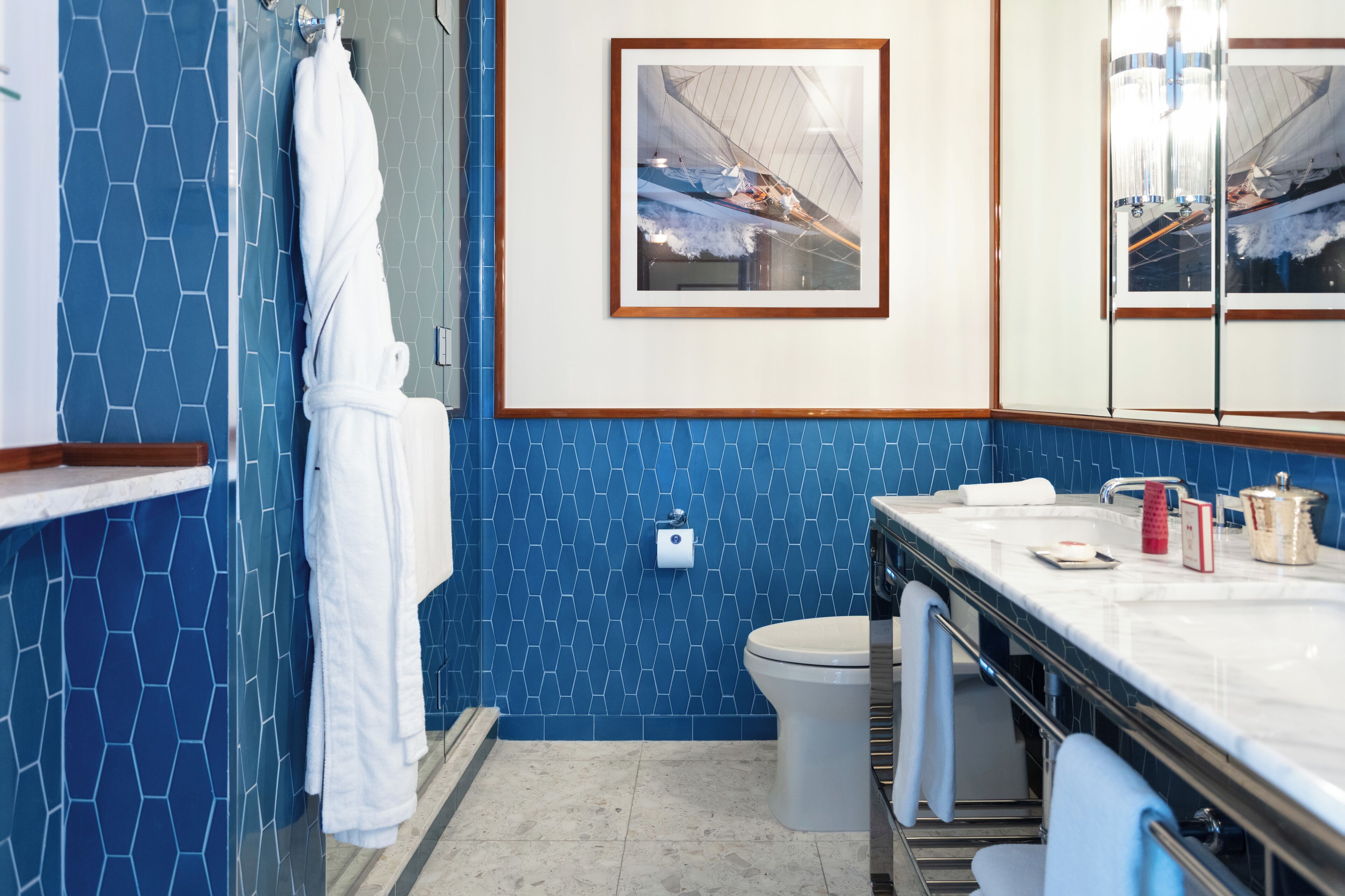 Un baño con pared de azulejos hexagonales azules, una bañera blanca, un inodoro y un lavabo con artículos de aseo.