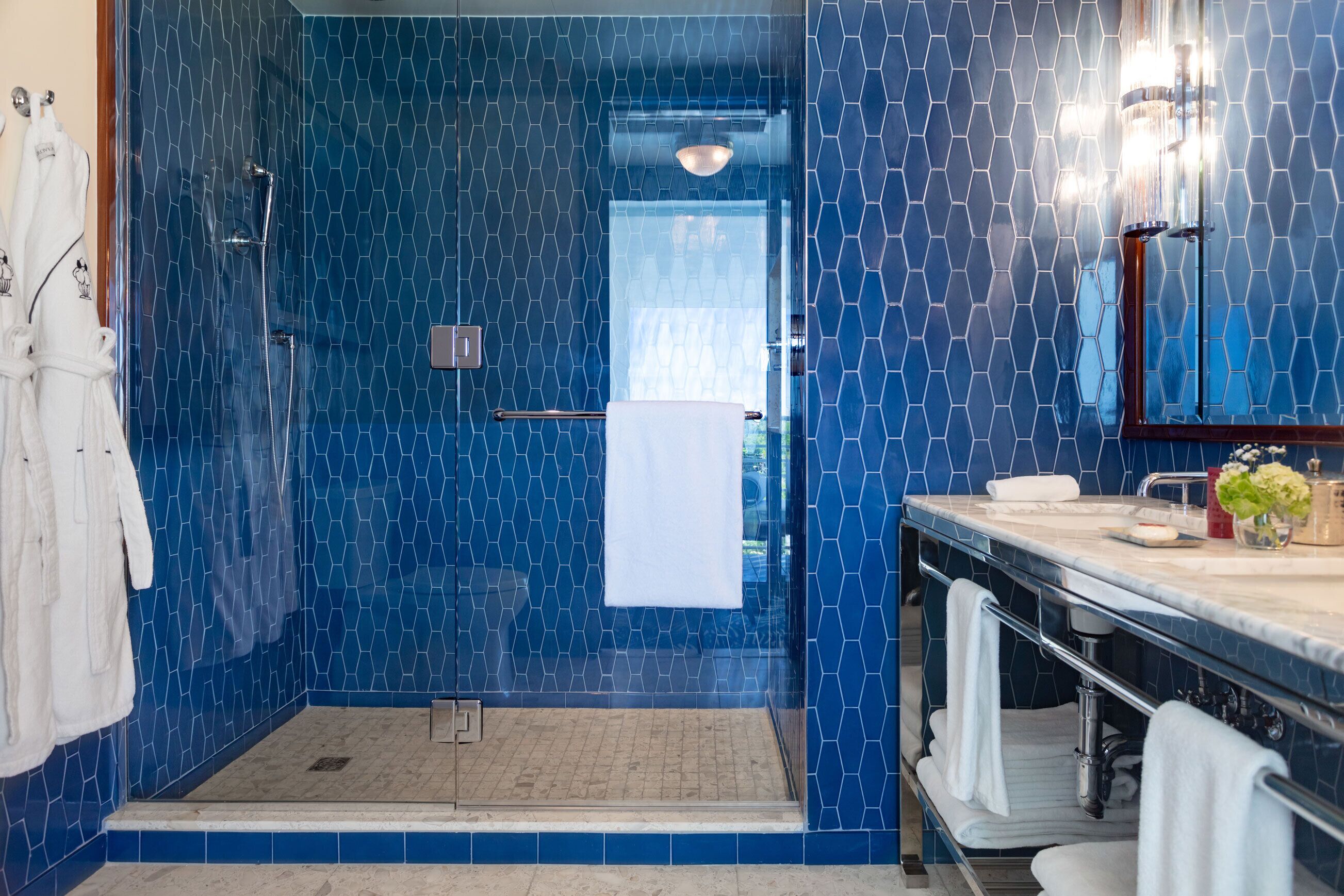 Uma casa de banho com cabine de duche em vidro, lavatório com espelho e porta-toalhas.